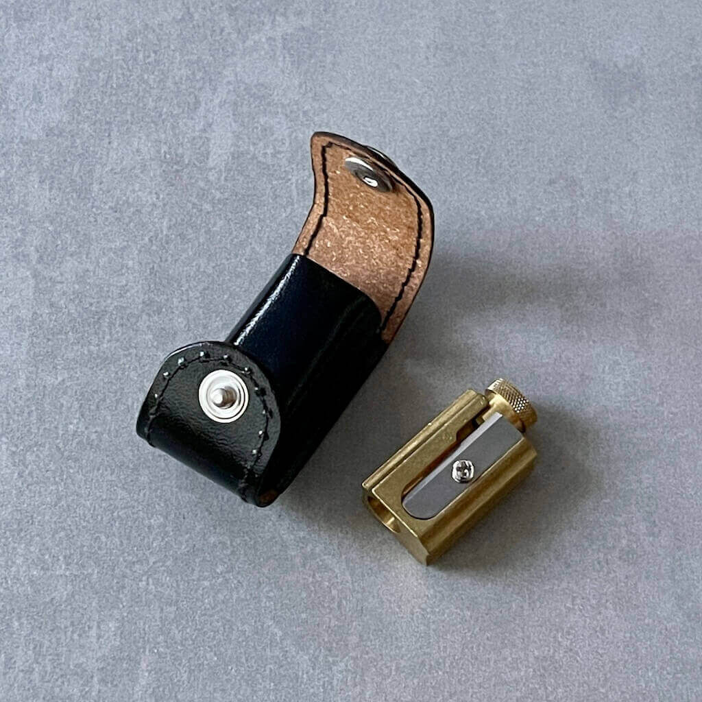 Gold metal pencil sharpener and black leather case on a gray surface