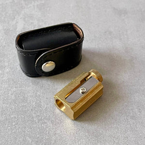 Gold metal pencil sharpener and black leather case on a gray surface