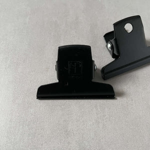 Two black clips by Ellepi on a gray background