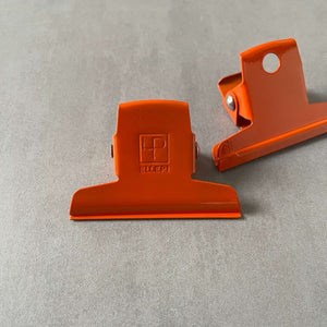 Two orange clips by Ellepi on a gray background