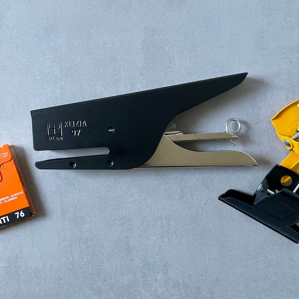 Black stapler with a box of staples and metal clips on a gray surface