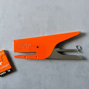 Orange stapler with a small box of staples on a gray background