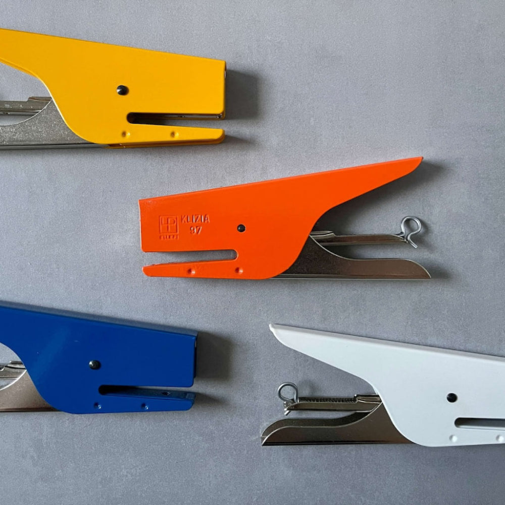 Four colorful staplers (yellow, orange, blue, white) on a gray background