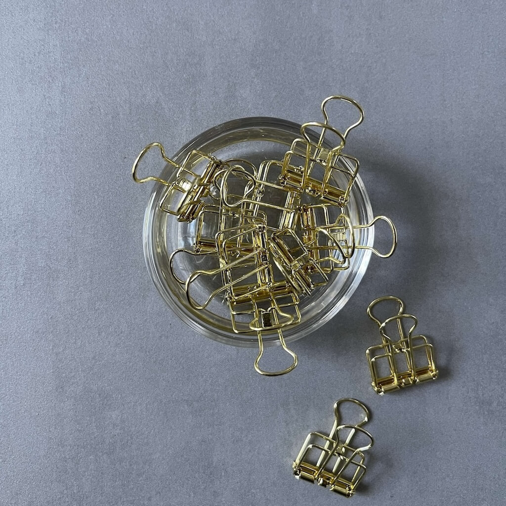 Gold binder clips on a clear glass dish against a gray background