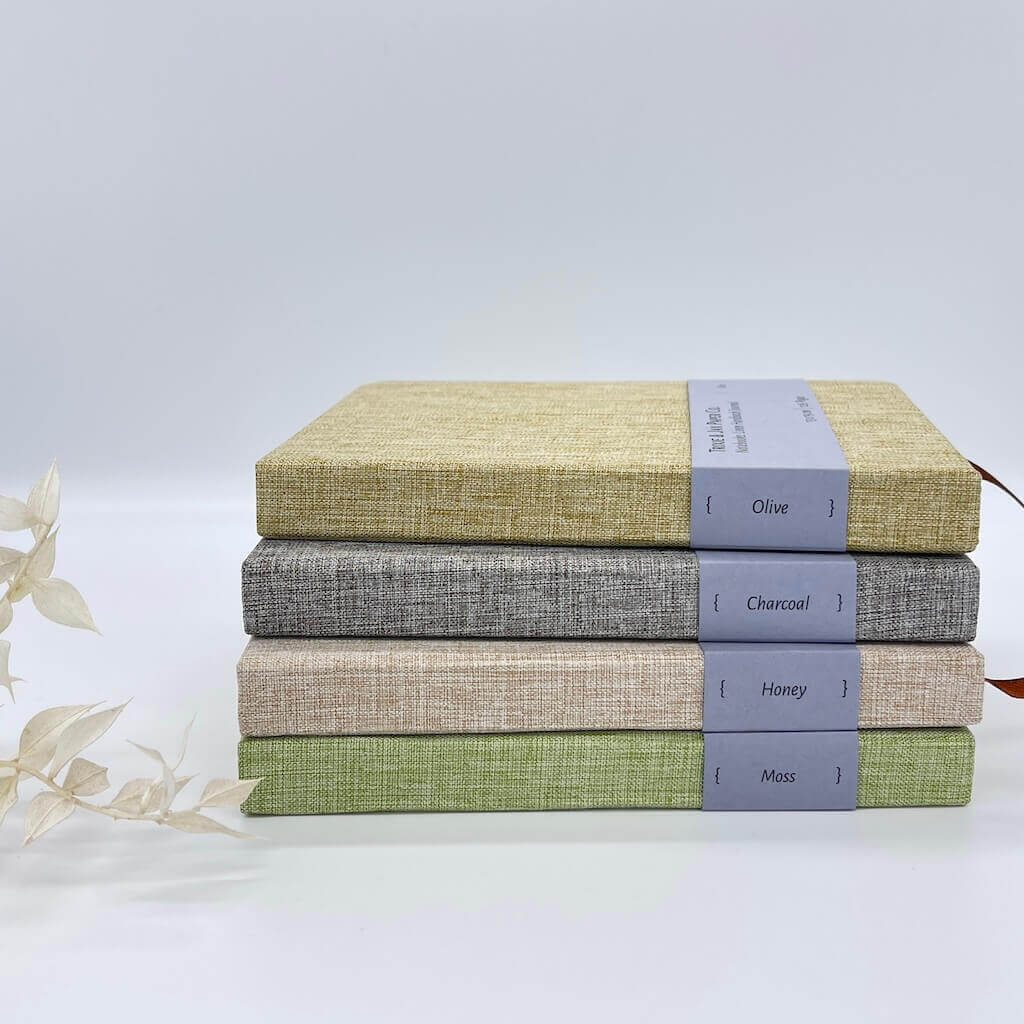 Stack of textured fabric books in gray, beige, and green on a white background