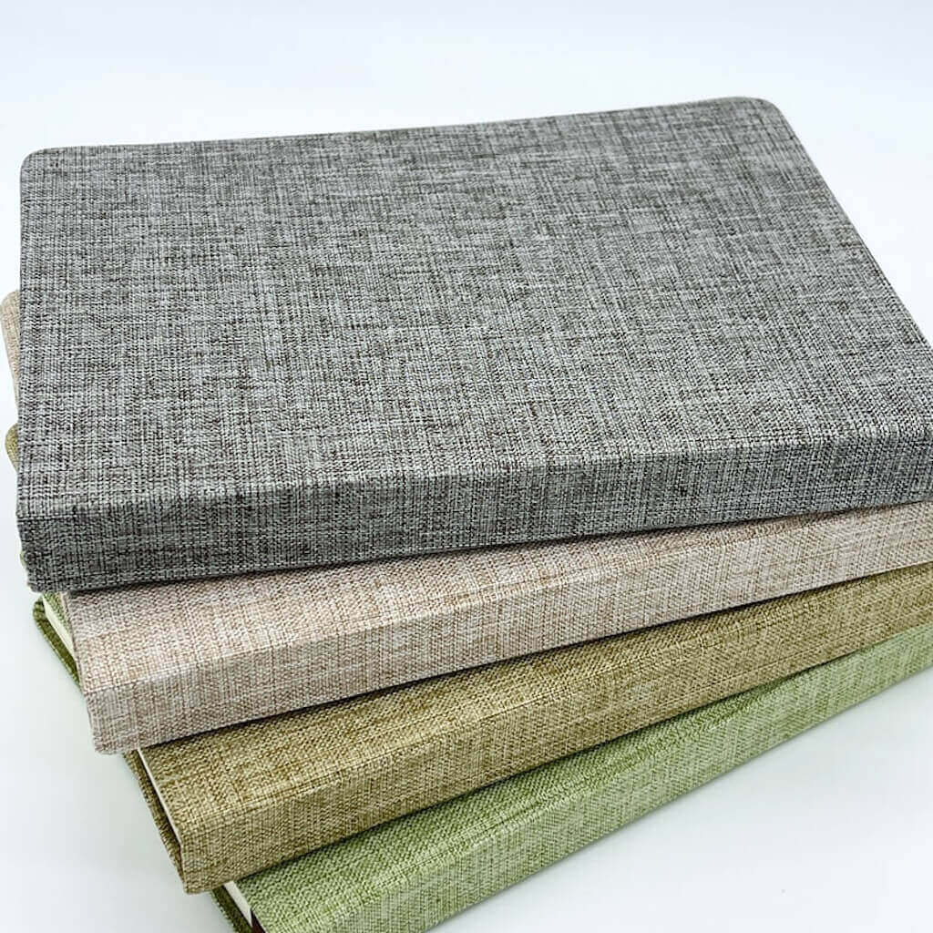 Stack of textured fabric books in gray, beige, and green on a white background
