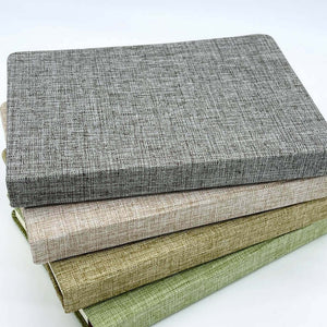 Stack of textured fabric books in gray, beige, and green on a white background