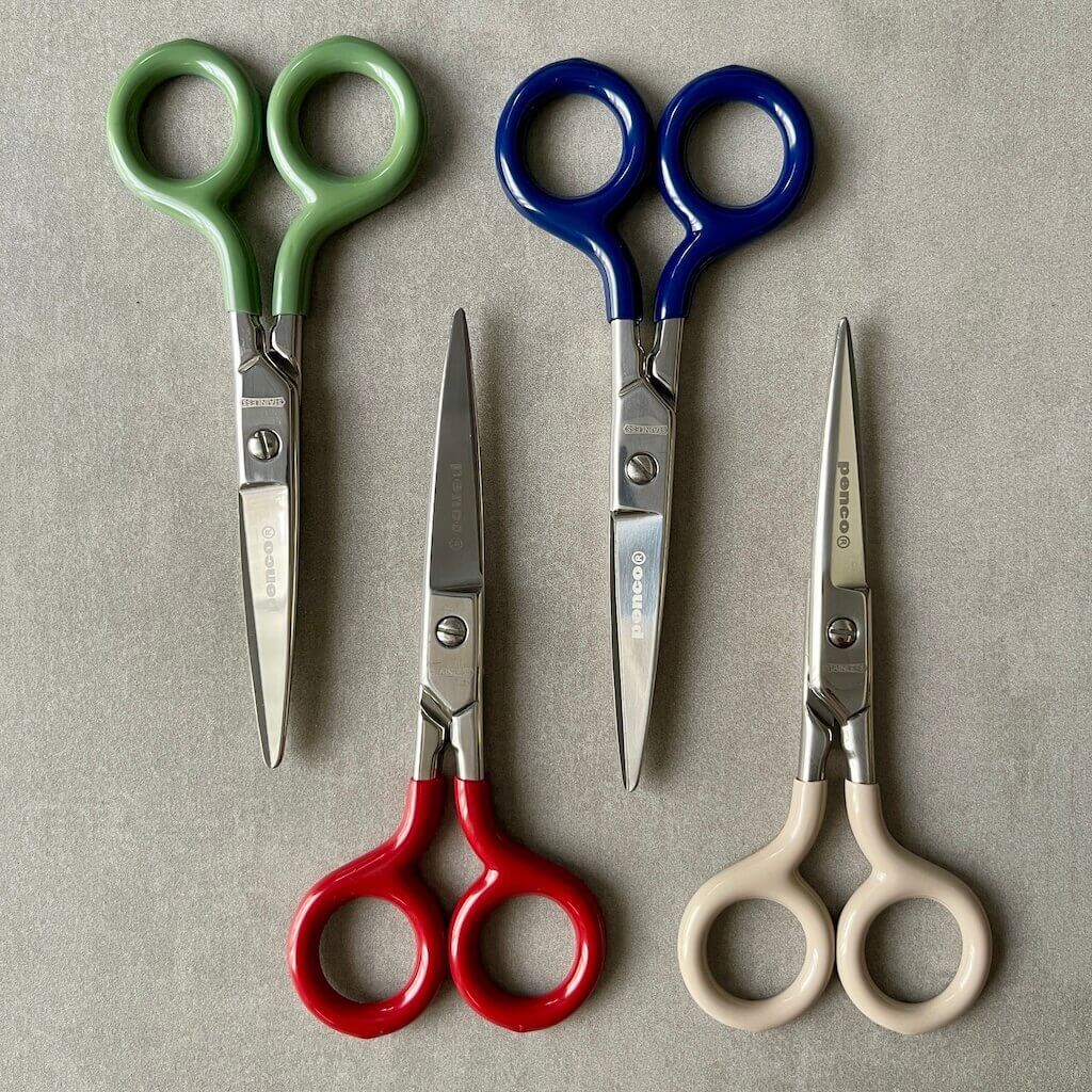 Four pairs of scissors with colored handles and 'Penco' brand on a gray background