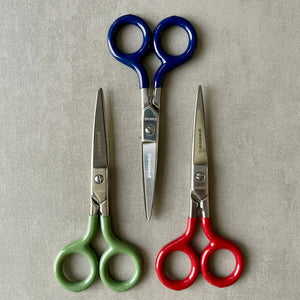 Three pairs of 'Penco' brand scissors with blue, green, and red handles on a beige background
