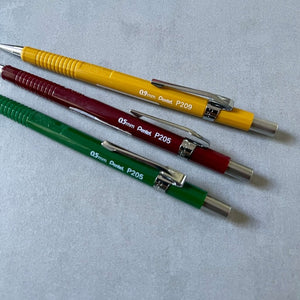 Three Pentel  Sharp mechanical pencils in yellow, red, and green on a light gray background
