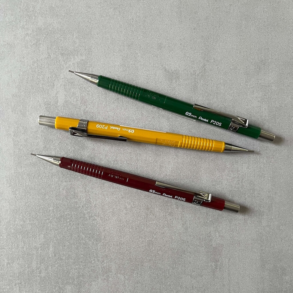 Three mechanical pencils in different colors on a gray background