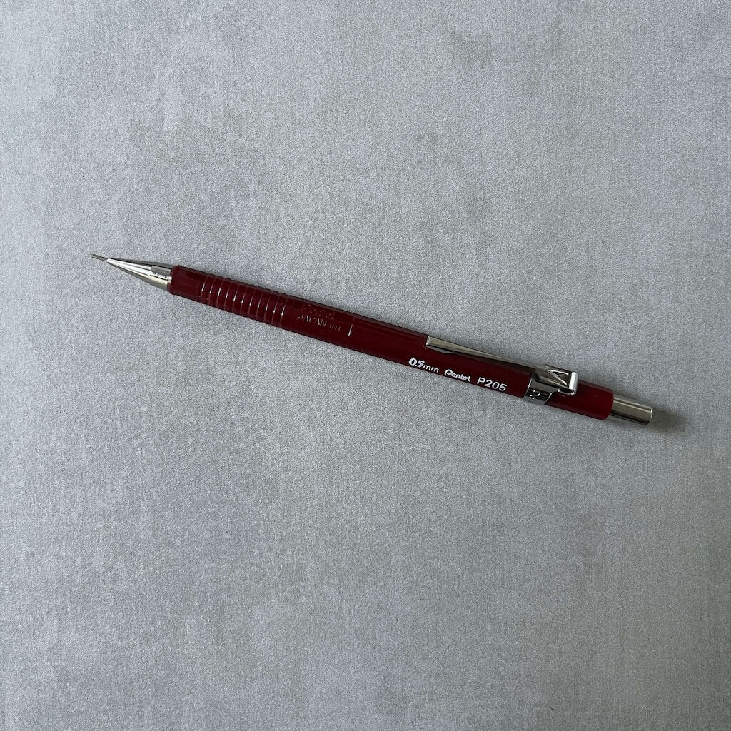 Red Pentel Sharp mechanical pencil on a gray textured background