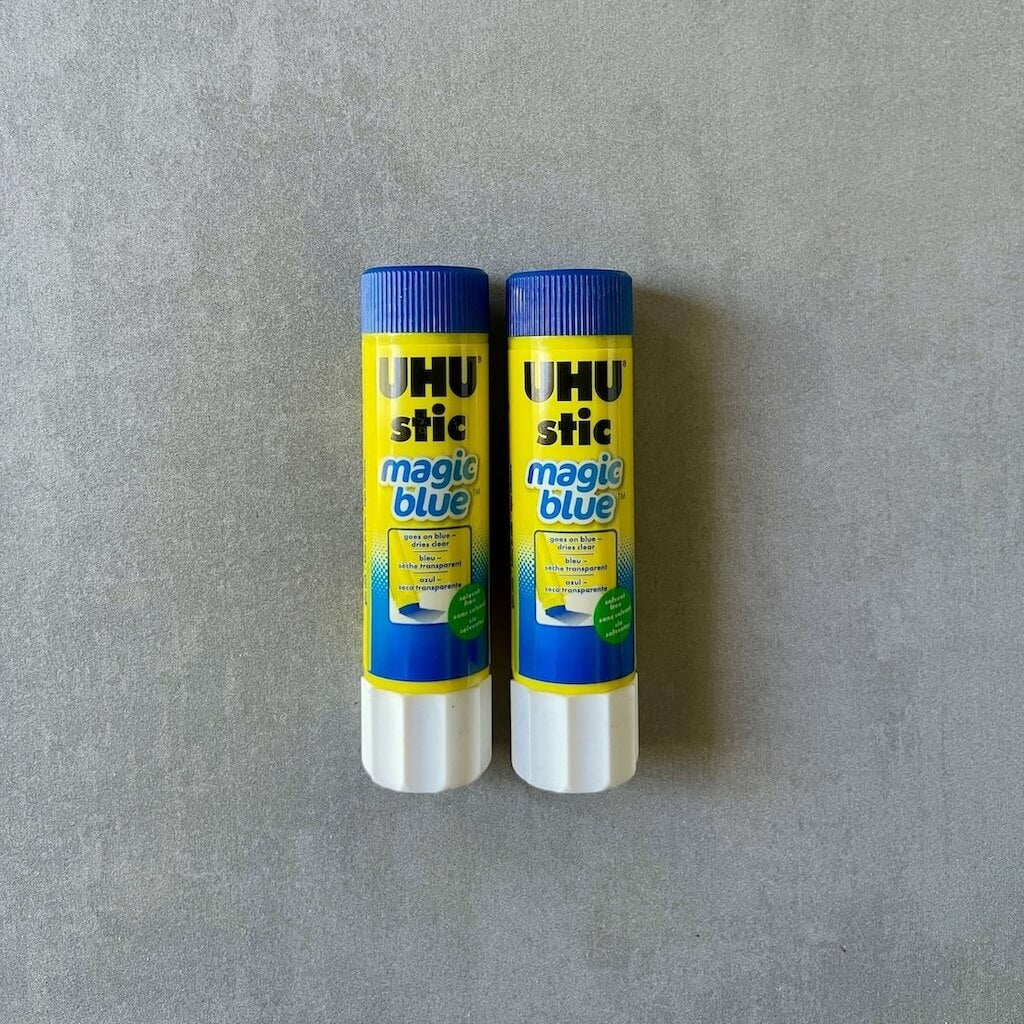 Two UHU stic magic blue glue sticks on a gray background
