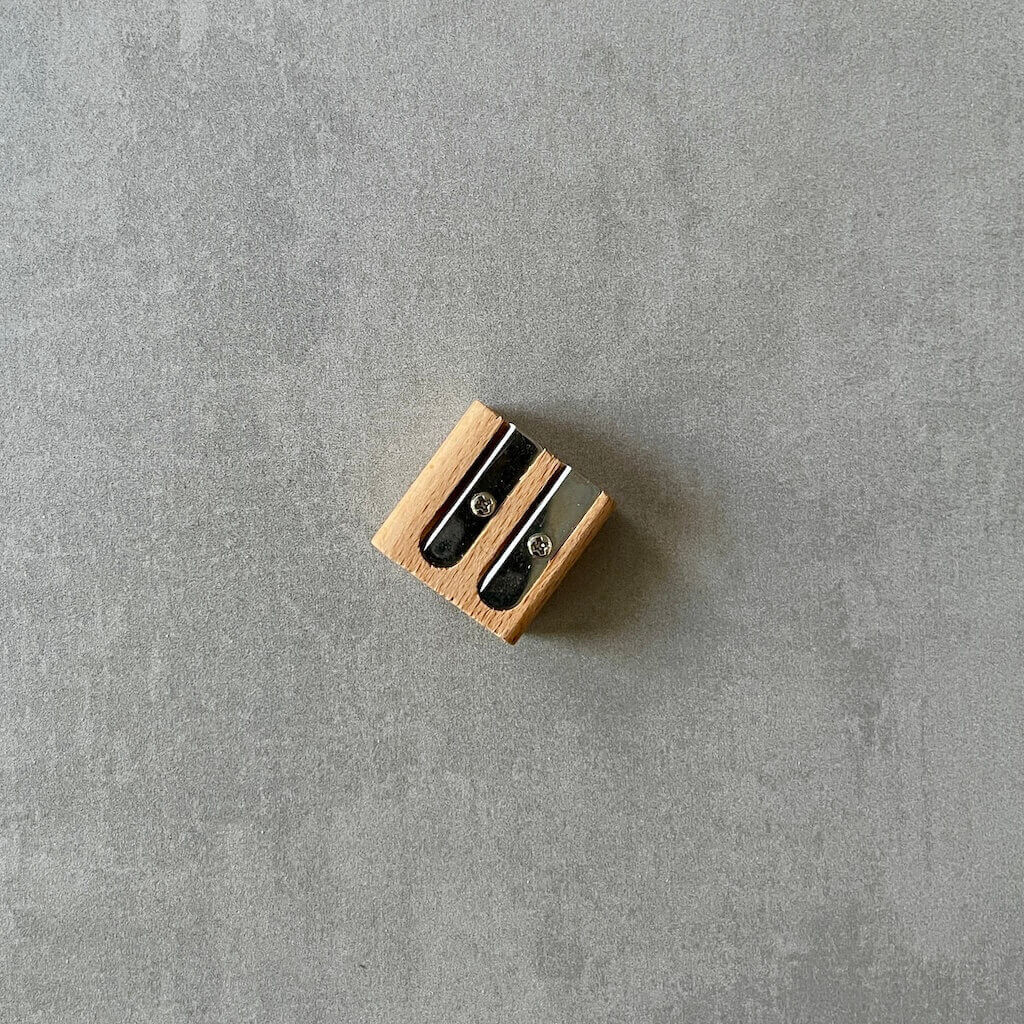 Small wooden pencil sharpener with two openings on a gray surface.