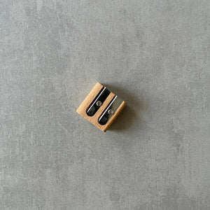 Small wooden pencil sharpener with two openings on a gray surface.